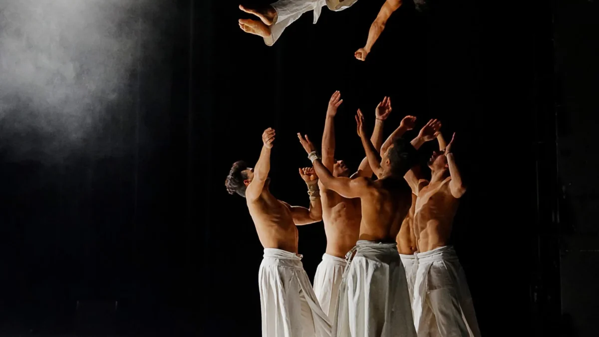 Grupo de 4 bailarines cn pantalon blanco y sin camiseta, lanzando al aire a un quito integrante