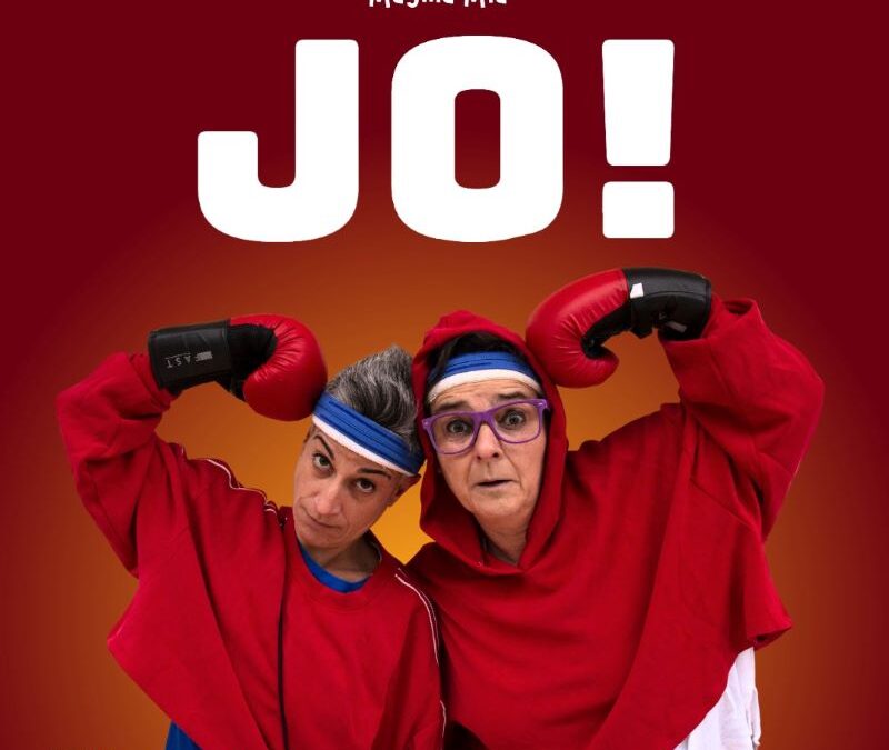 Dos mujeres con ropa deportiva y guantes de boxeo en el centro de la imagen. El brazo extrerior de cada una de ellas esta apoyado en la sien con el guante de boxeo. Ambas llevan una cinta azul en la frente para retener el sudor. La de la izquierda con gafas de pasta moradas y la capucha de la sudadera roja puesta.