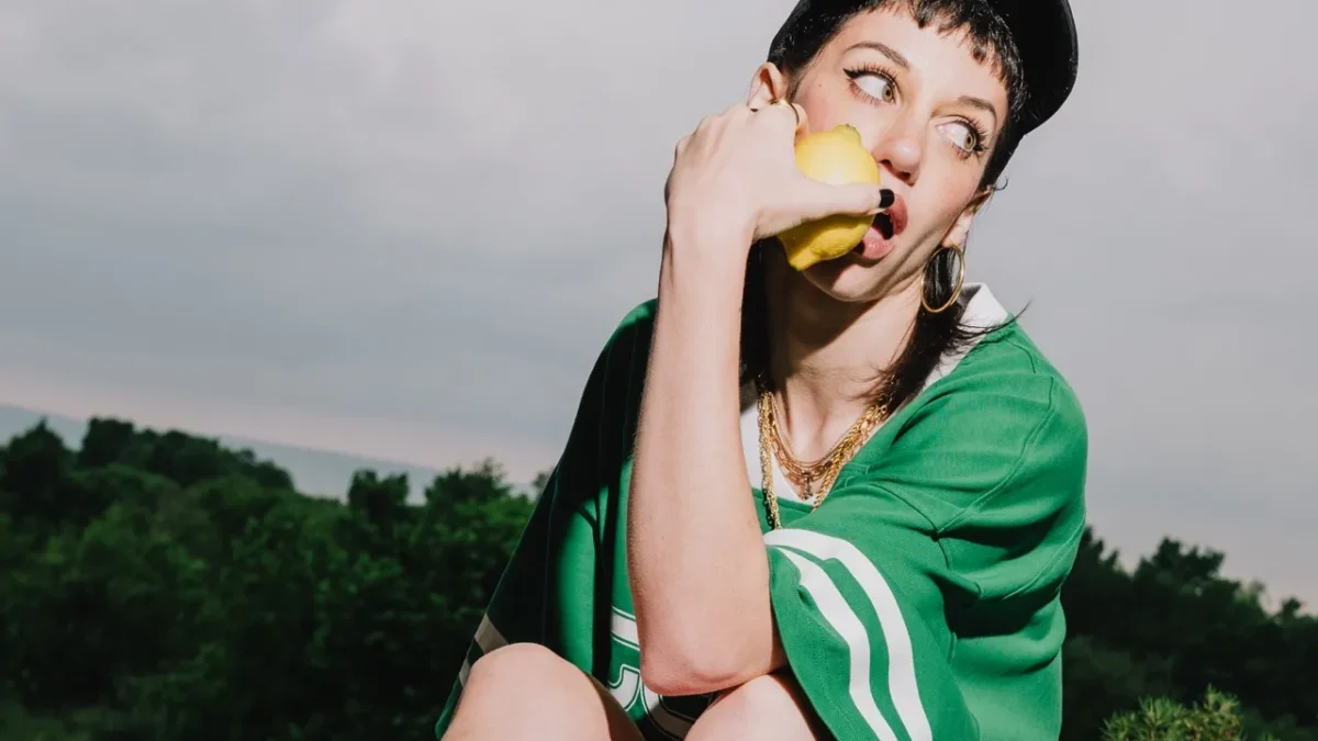 imagen de una mujer de estilo urbano, sentada, con una gorra mirando al lateral mordiendo un limon.